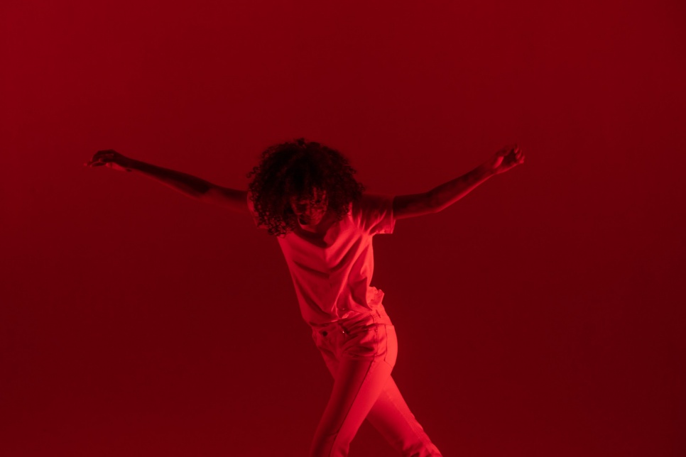 A person with arms stretched out dancing with red lighting as background