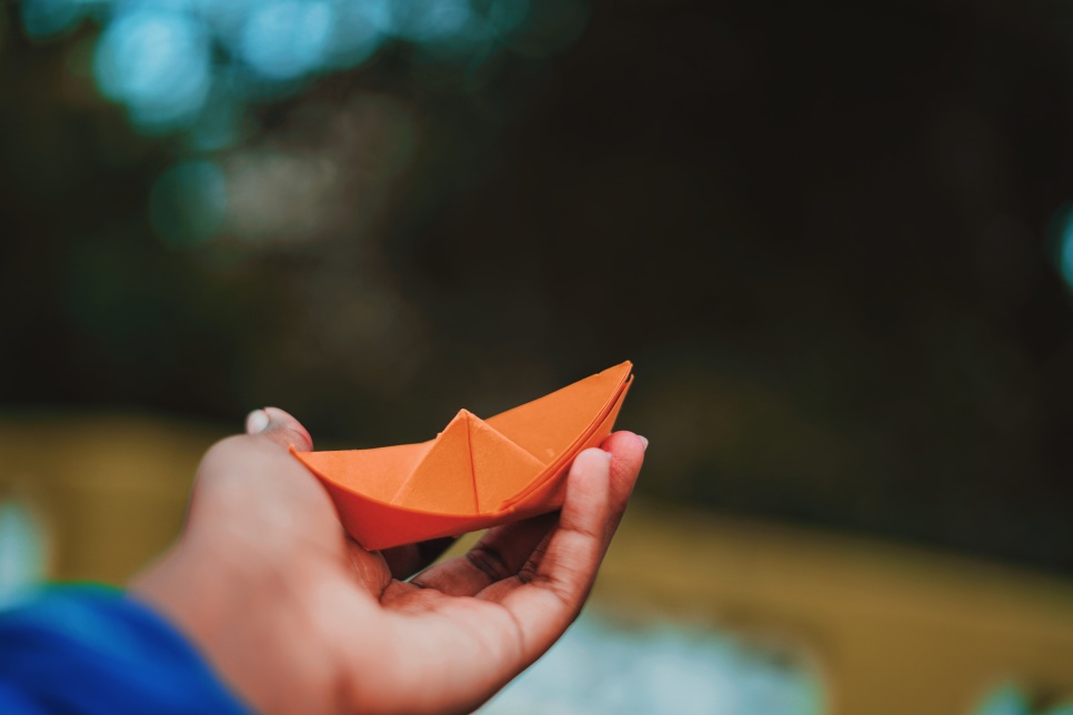 Hand outstretched is holding an orange origami boat
