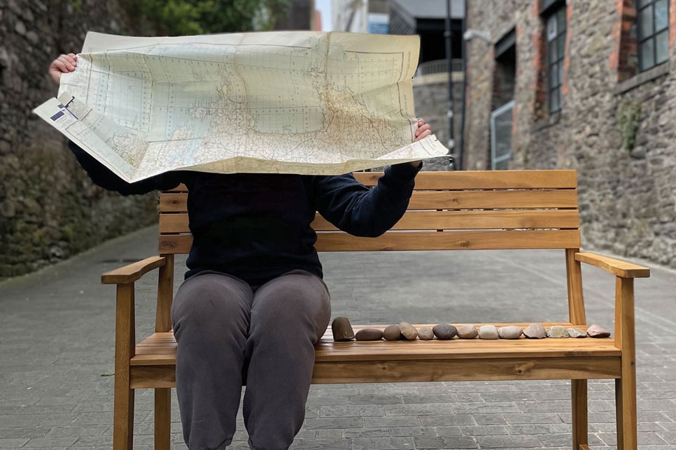 A person sat on a bench with their face hidden behind a large map