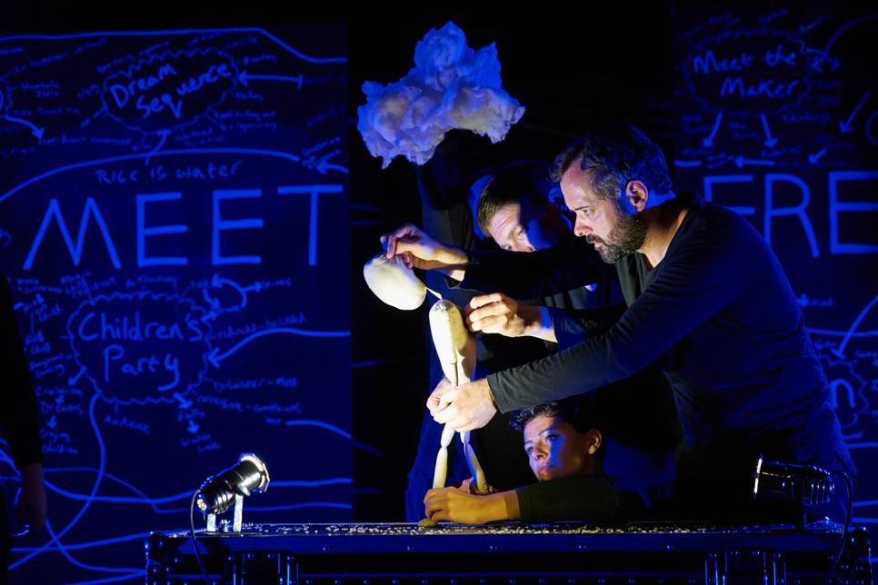Two actors hold a puppet on a stage.