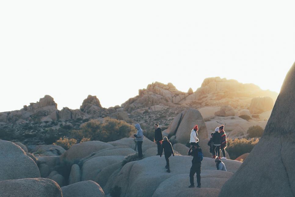A group of people stand on big rocks outside as the sun sets