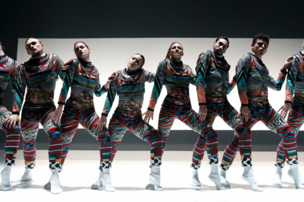 8 dancers lined up on stage in colourful bodysuits