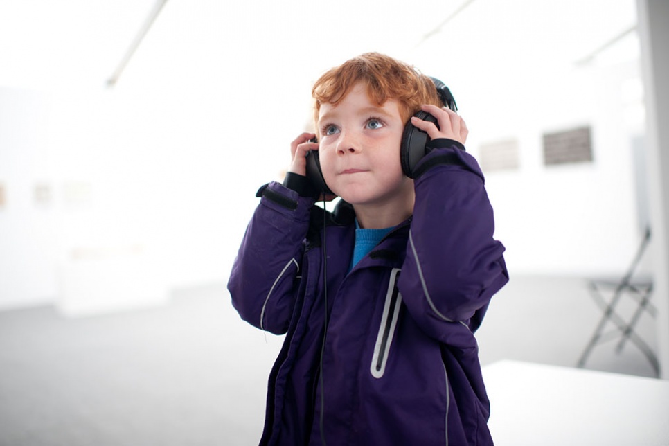 Boy with headphones on stands in a white gallery