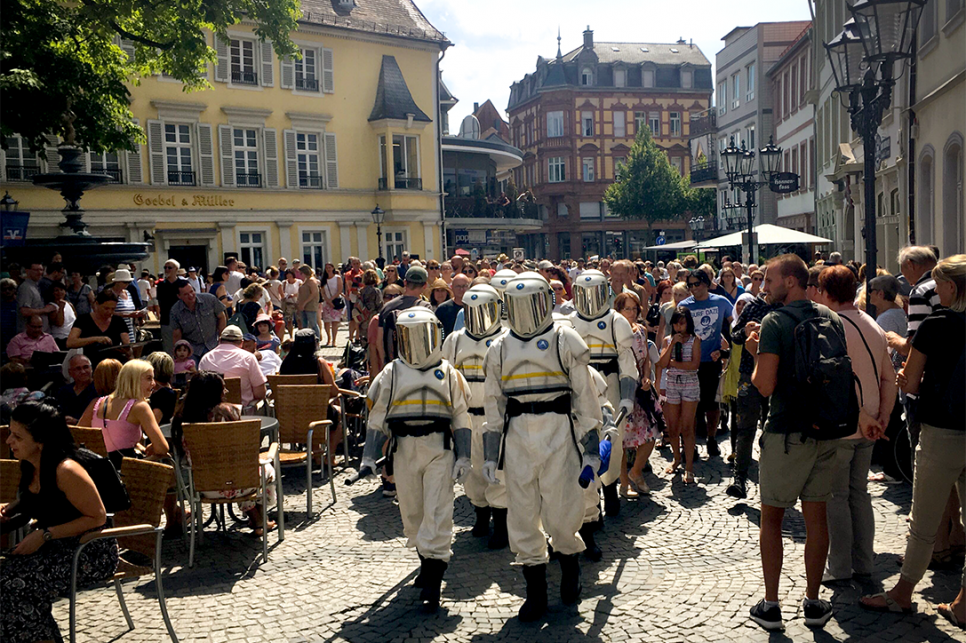 Hijinx_The Astronauts_Kaiserslautern_2019 Astronauts walking through crowds in a picturesque German town