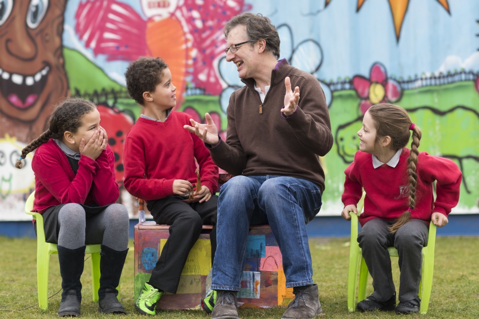 Image of three pupils and an adult sitting on chairs with a colourful mural behind them