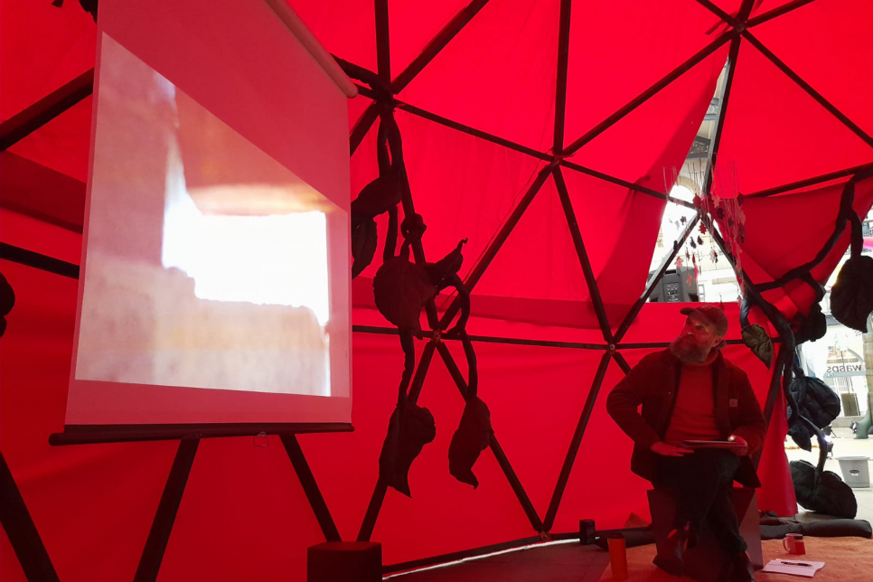 A person sat on a stool within a red dome looking at a screen with an image projected on it