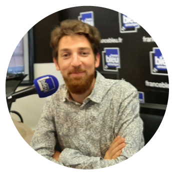 Lors Jereg wearing a patterned shirt in a radio studio with a microphone.