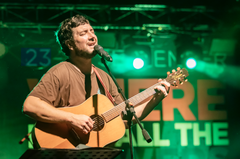 Gareth Bonello performing onstage with a guitar, green stage lighting in the background