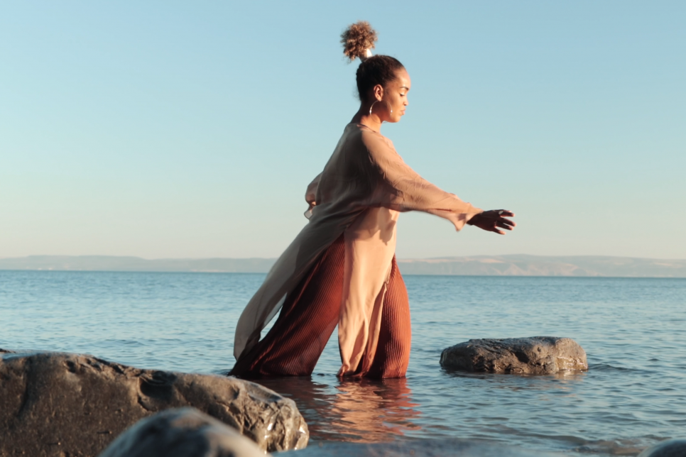 Lady dancing in the sea with flowing clothes and skyline in the background