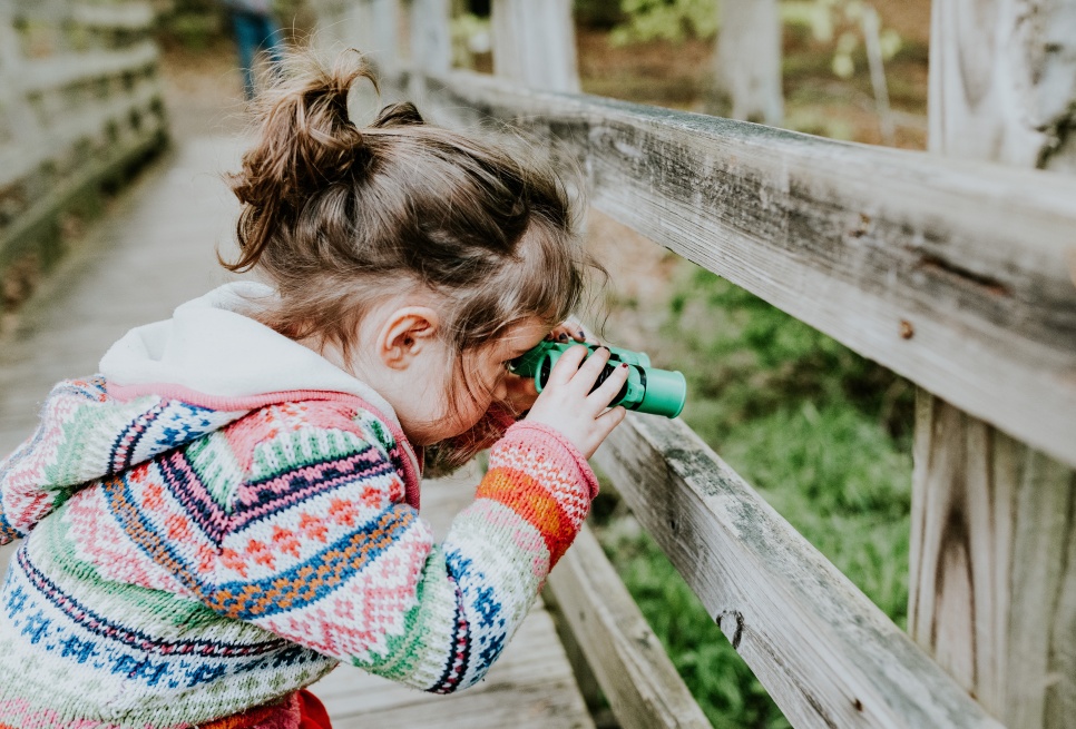 A child in a colourful cardigan looking through small binculars