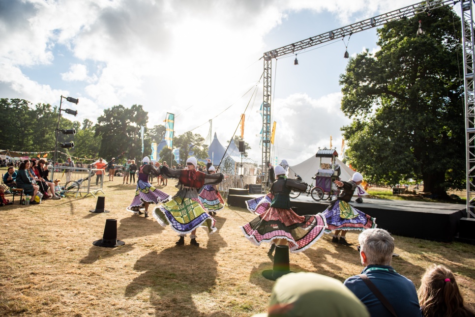 Performers in colourful dresses, dancing outside at the Eisteddfod in the sunshine.