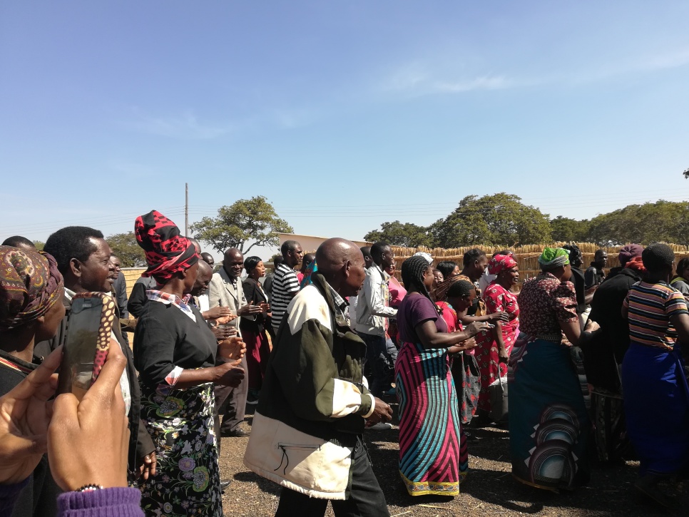Credit: Chembo Liandisha Group of people walking from left of screen to right of screen, some in traditional outfits