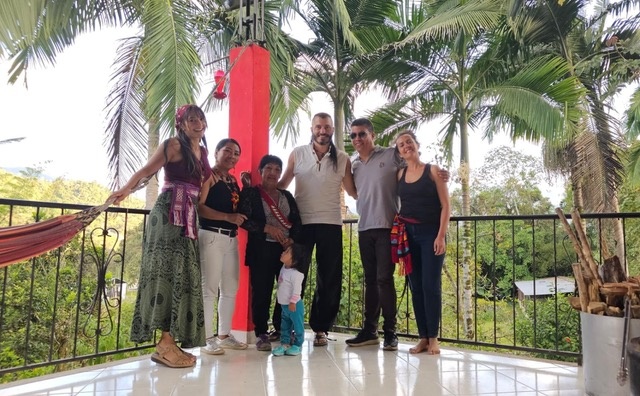 Credit: Georgina Biggs 6 individuals standing on a balcony with black metal bars with palm trees in the background