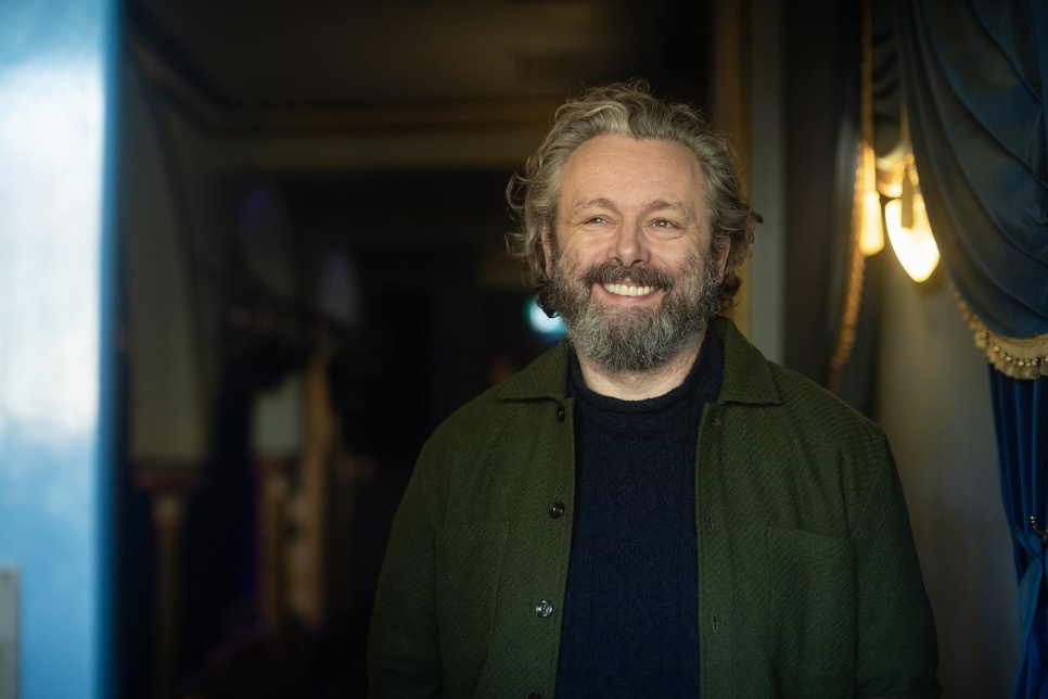 A head and upper body shot of Michael Sheen who is smiling