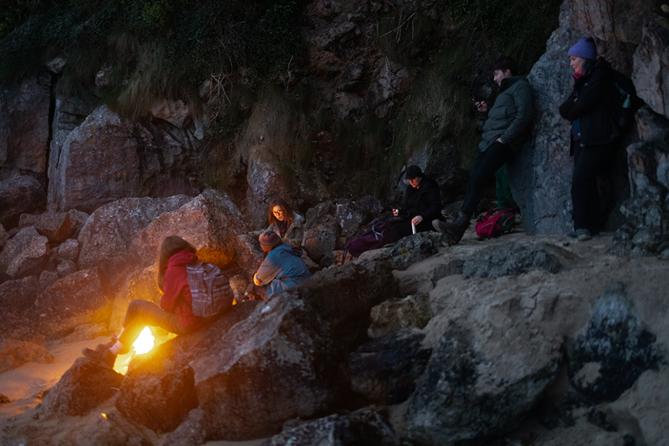 people sitting on a rock at nightime around a fire