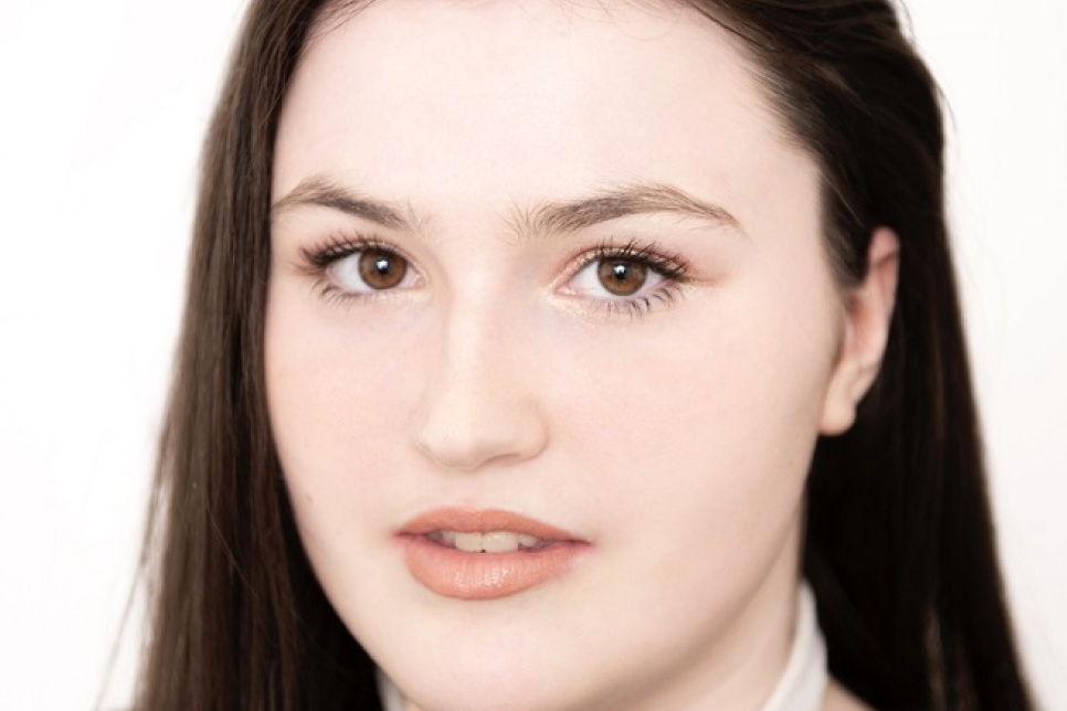 Headshot of Tonia, a young disabled freelance dancer at Ballet Cymru. She has long dark hair and wears a black top. She has a tube fitted on her neck to aid breathing and food intake.. 