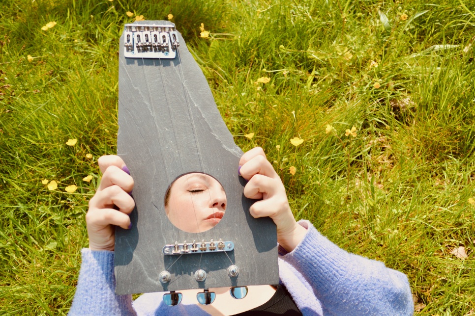 Image of the artist holding a handmade slate instrument / Delwedd o'r artist yn dal offeryn wedi ei wneud â llaw o lechen