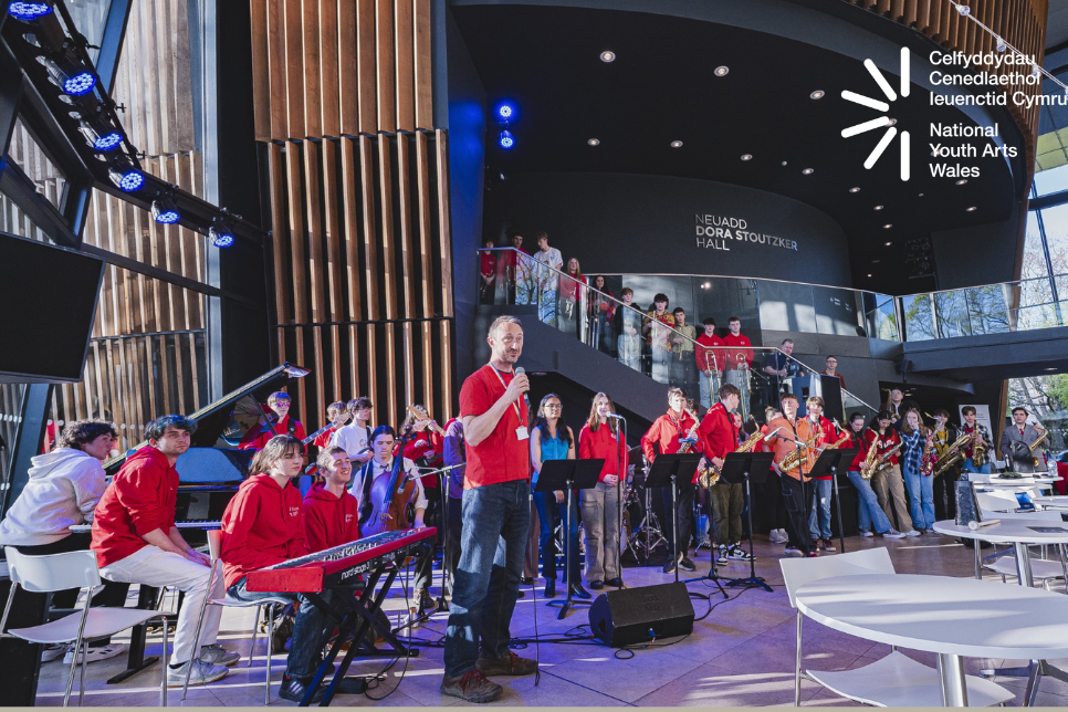 Mae Jazz Cenedlaethol Ieuenctid Cymru yn cael ei lansio yng Coleg Brenhinol Cerdd a Drama Cymru. Prif Weithredwr CCIC, Evan Dawson yn dal meicroffon yng nghanol y ddelwedd cyn i'r cerddorion ifanc berfformio. Llun gan: Kirsten McTernan.