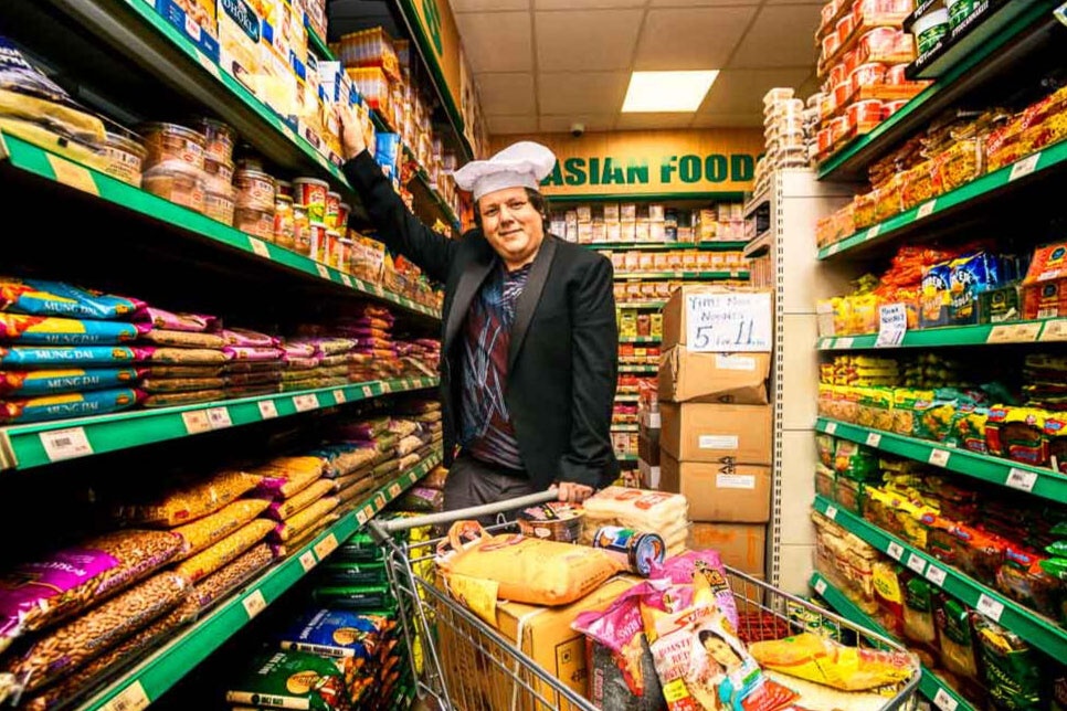 A person wearing a chef's hat behind a shopping trolley, in a supermarket aisle.