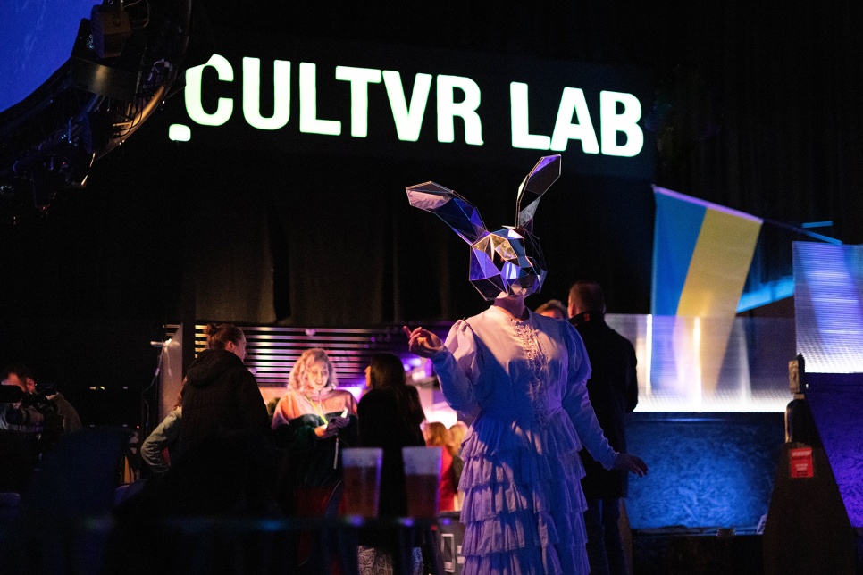 A performer with a head mask in front of the CULTVR Lab sign / Perfformiwr gyda mwgwd pen o flaen arwydd CULTVR Lab 