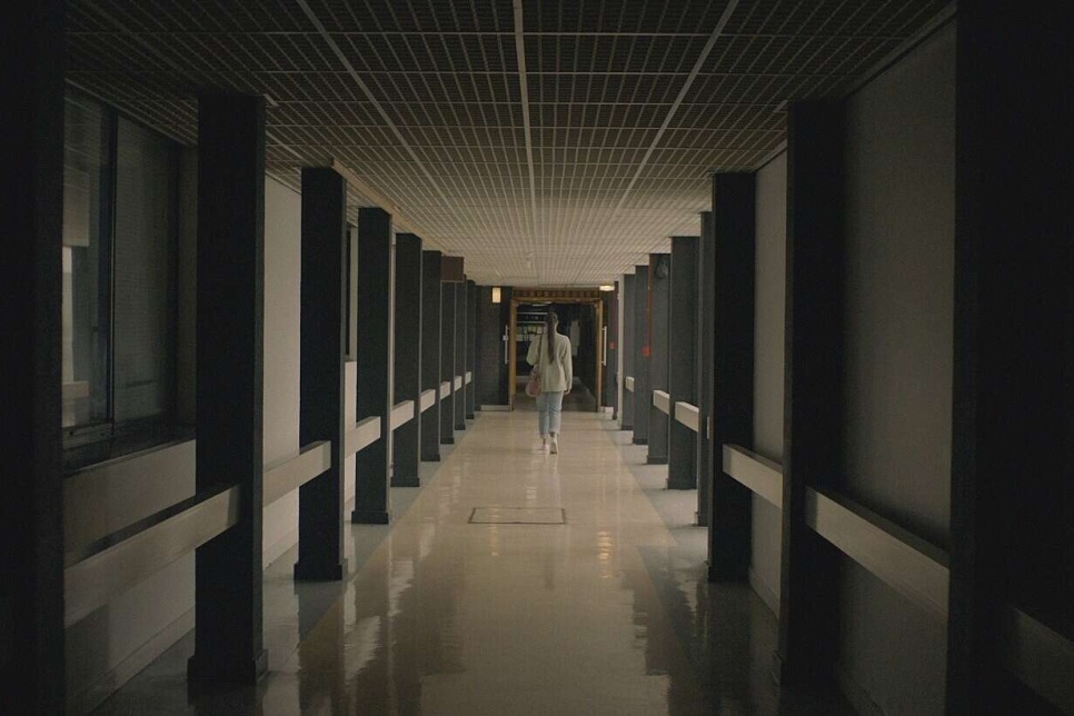 Image - A film still of a corridor with a person walking away from the camera / Delwedd - ‘Stil’ ffilm o goridor gyda pherson yn cerdded i ffwrdd oddi wrth y camera