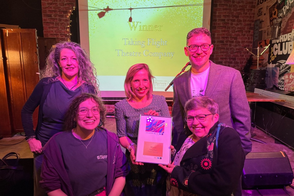 Photograph of five people looking straight at the camera at an awards ceremony. Two are holding a framed certificate between them. / Ffotograff o bump o bobl yn edrych yn syth at y camera mewn seremoni wobrwyo. Mae dau yn dal tystysgrif mewn ffrâm rhyngddyn nhw.