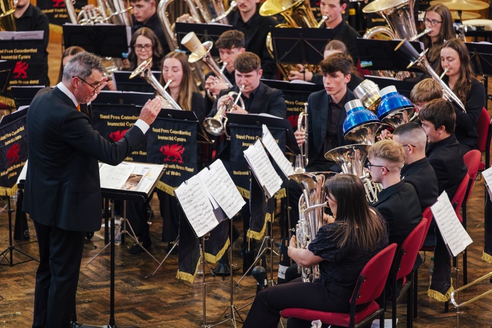 A conductor and orchestra members performing / Arweinydd ac aelodau cerddorfa yn perfformio